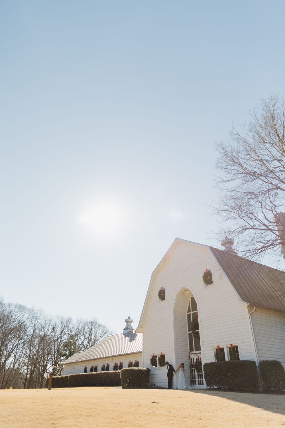 White barn-style wedding venue with arched roof photographed against blue sky.