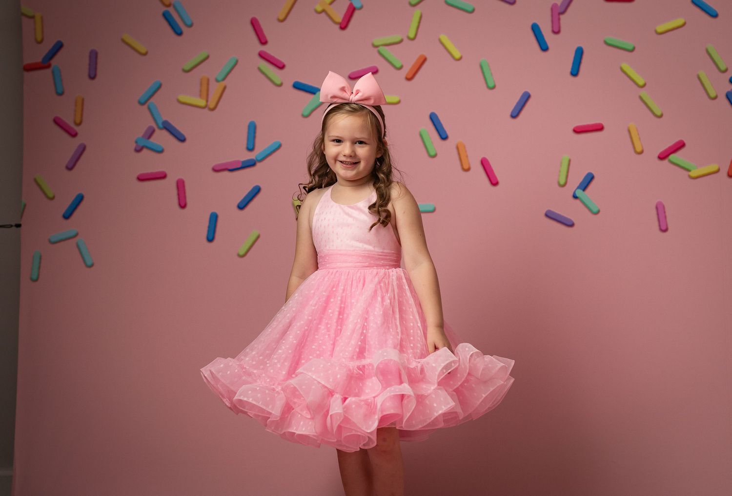 Twirling pink tulle dress photographed against soft pastel clouds background.