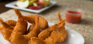 Golden fried butterfly shrimp served with cocktail sauce on a white plate against a neutral background.