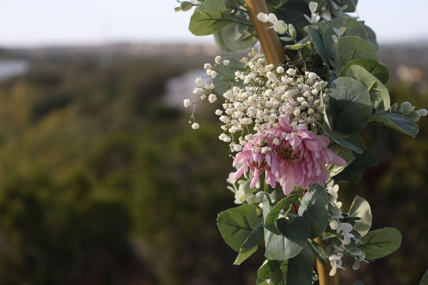 A pink peony flower arrangement with baby's breath and eucalyptus leaves against a blurred outdoor background.