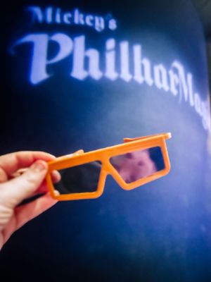 Orange safety glasses are held against a dark blue background with text illuminated in the distance.