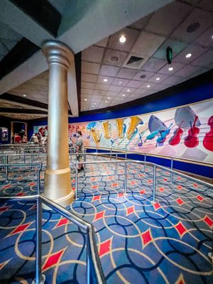 Vibrant Disney cruise ship interior with geometric blue carpet, gold column, and colorful character-themed wall art.