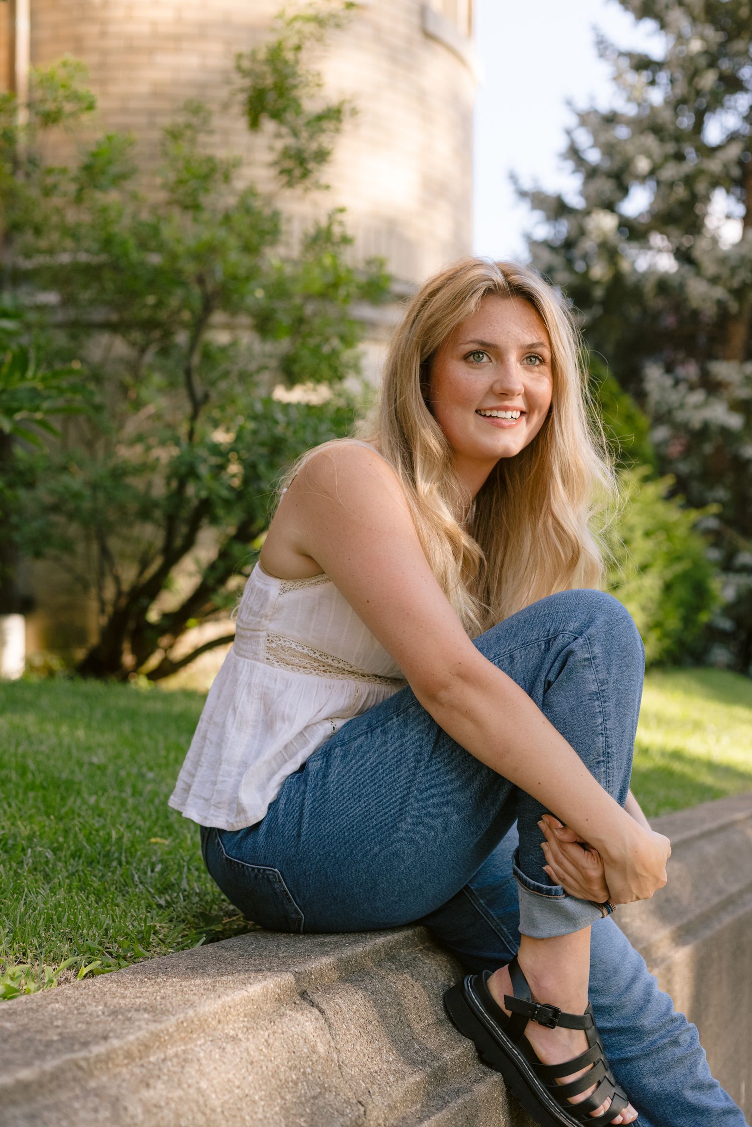 Relaxed outdoor portrait on stone steps with brick building and trees in background.