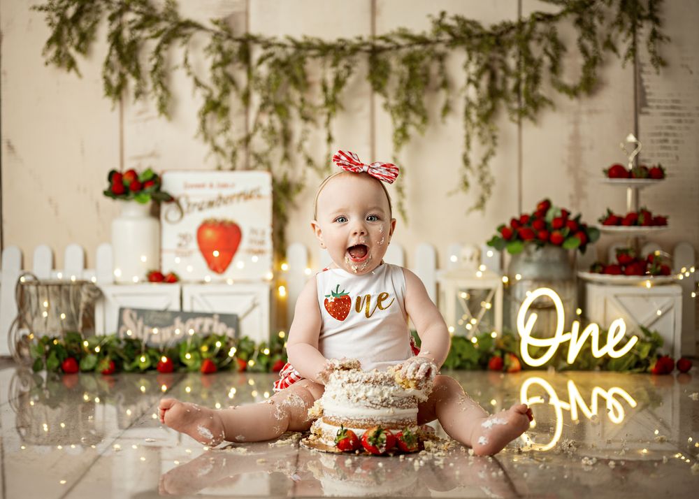 First birthday cake smash photography setup with festive Christmas decor, glowing lights and pine garland decorations.
