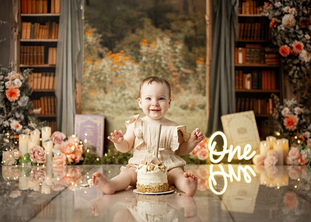 Baby's first birthday setup with rustic bookshelves, floral decorations and a gold 'One' sign for cake smash photography.