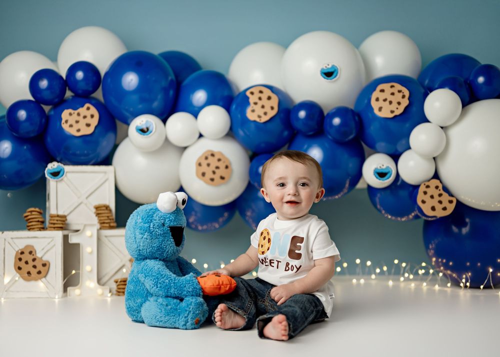 Milk and cookies themed birthday party setup with blue and white balloons, fairy lights, and plush Cookie Monster decor.