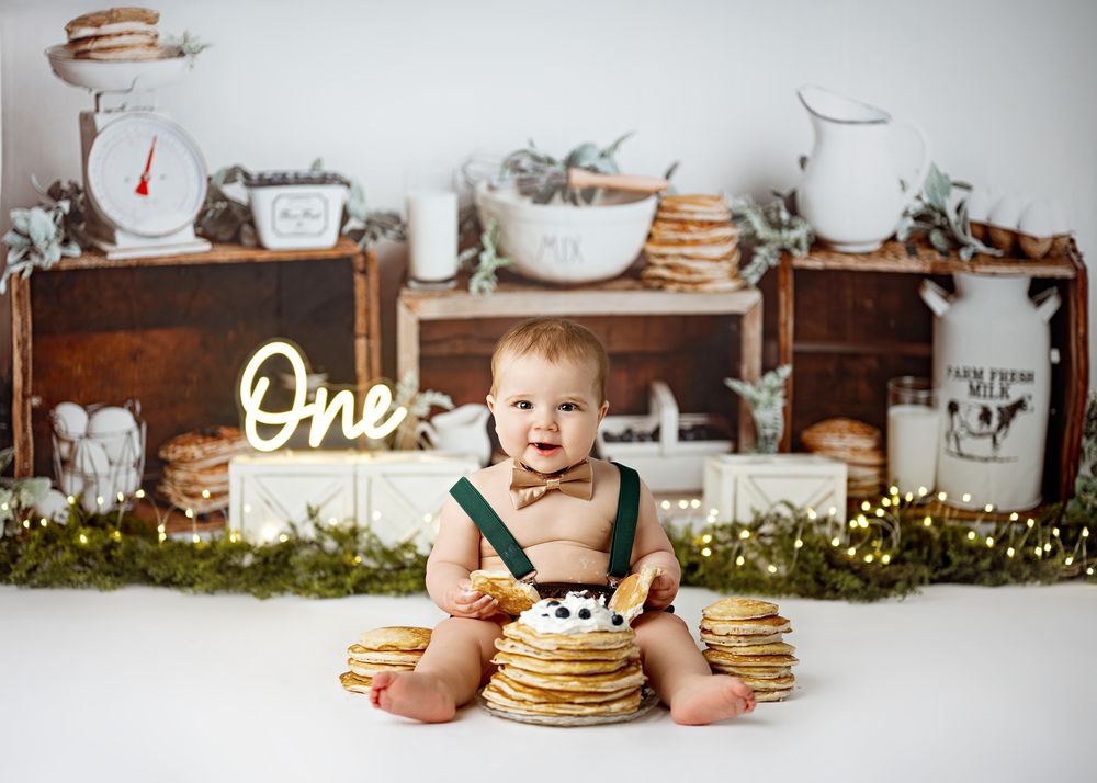 Rustic cake smash setup with pancakes, flowers and vintage decor featuring neon 'One' sign.