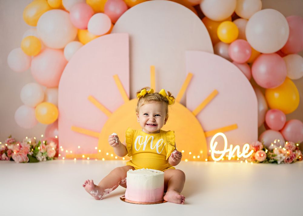Pink and gold balloon decor creates a festive backdrop for a first birthday cake smash photoshoot with glowing lights.