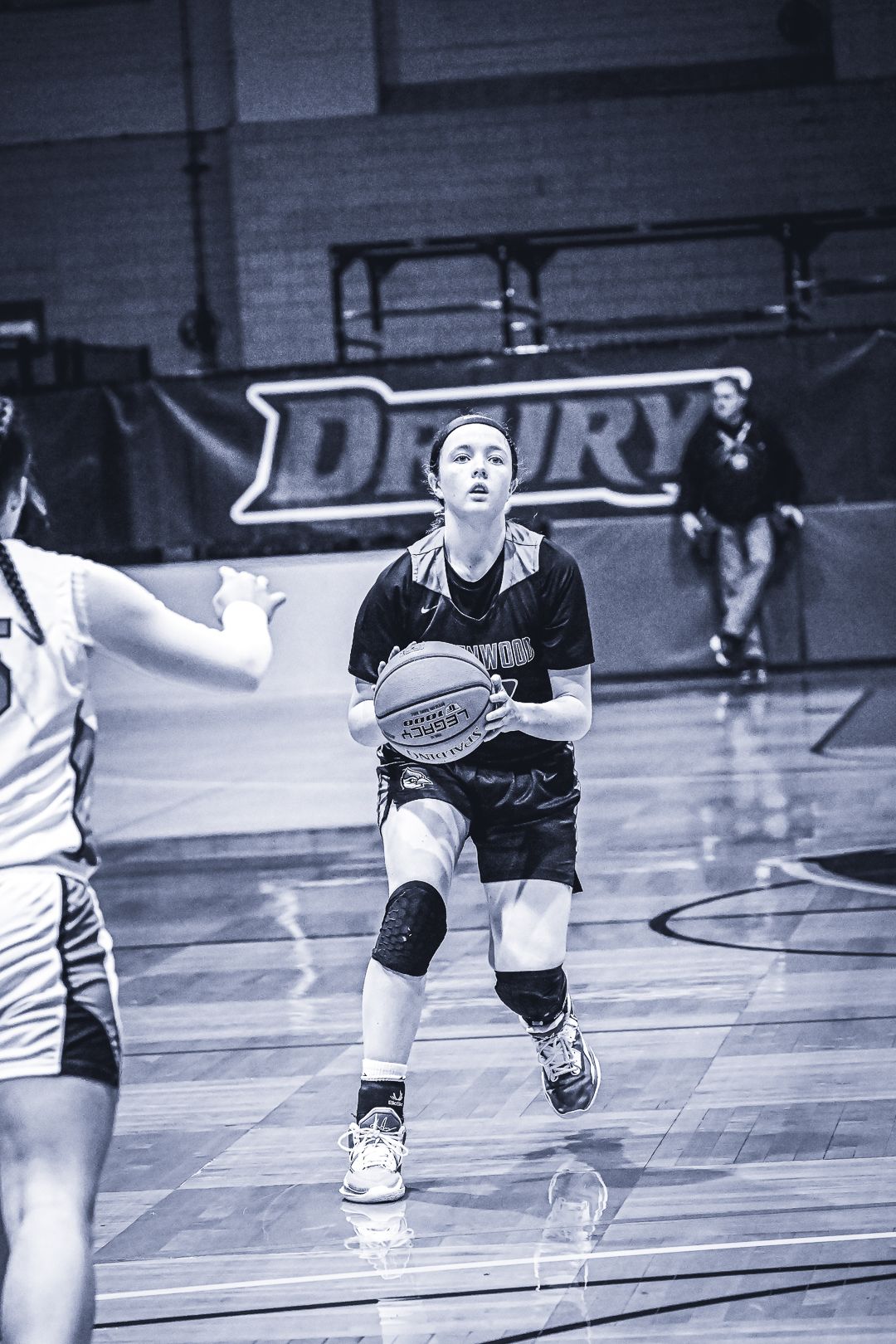 Basketball player dribbling down court during competitive game in gymnasium.