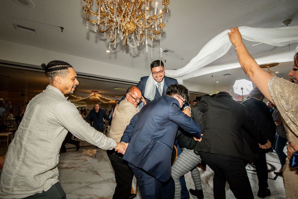 A group of people dancing energetically under an elegant crystal chandelier. Groom tossed during Víbora de la Mar Chicago.