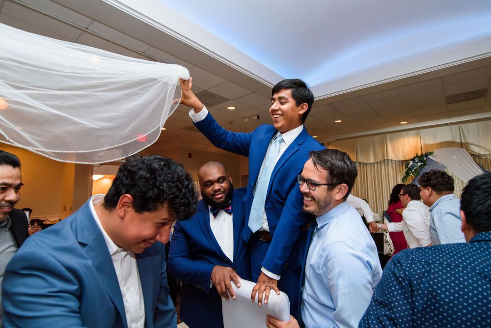 People celebrate at an indoor event with someone in a blue suit lifting up a white cloth. Mexican wedding celebrations in Chicago