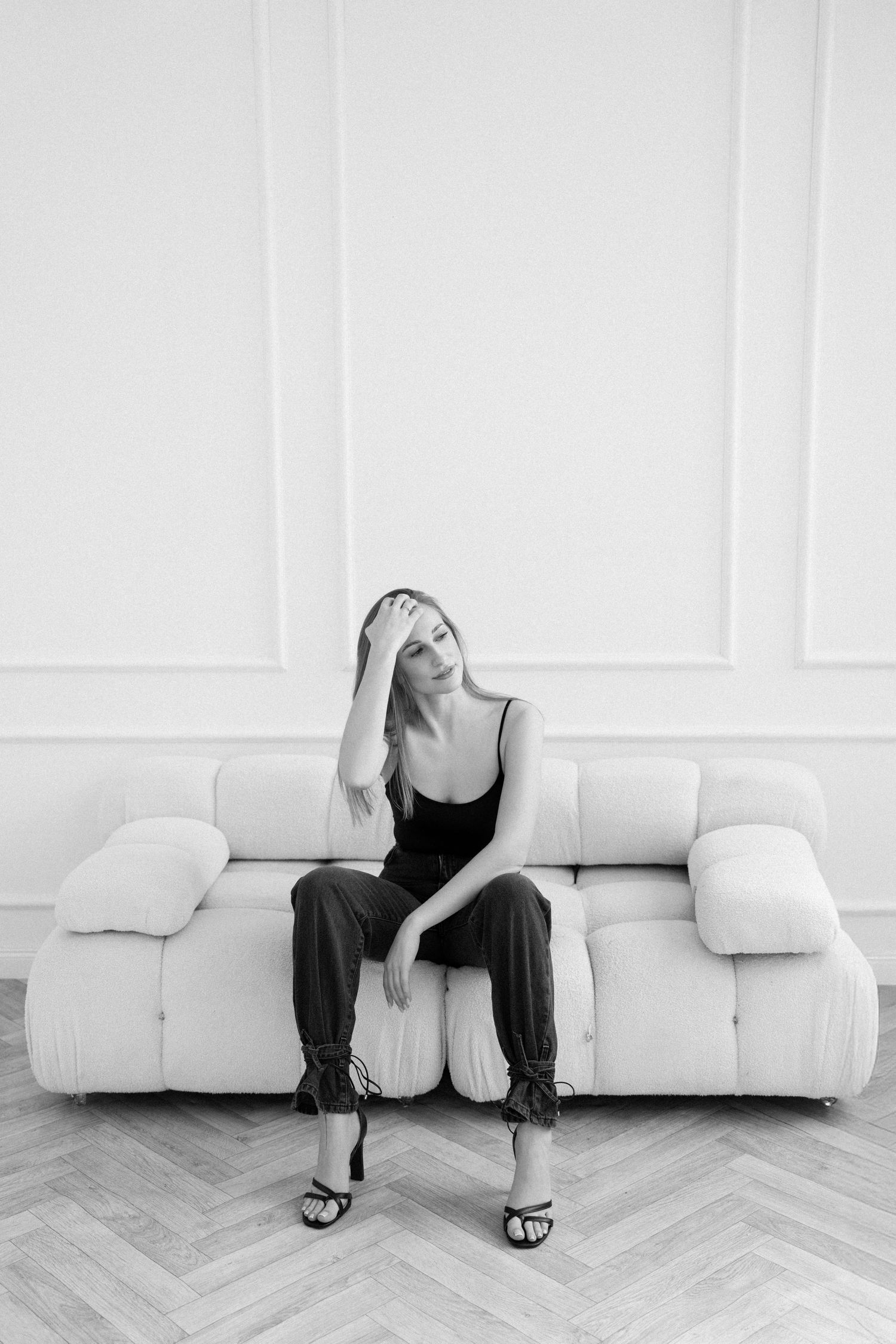 Black and white photo of person sitting casually on plush white couch in modern room.