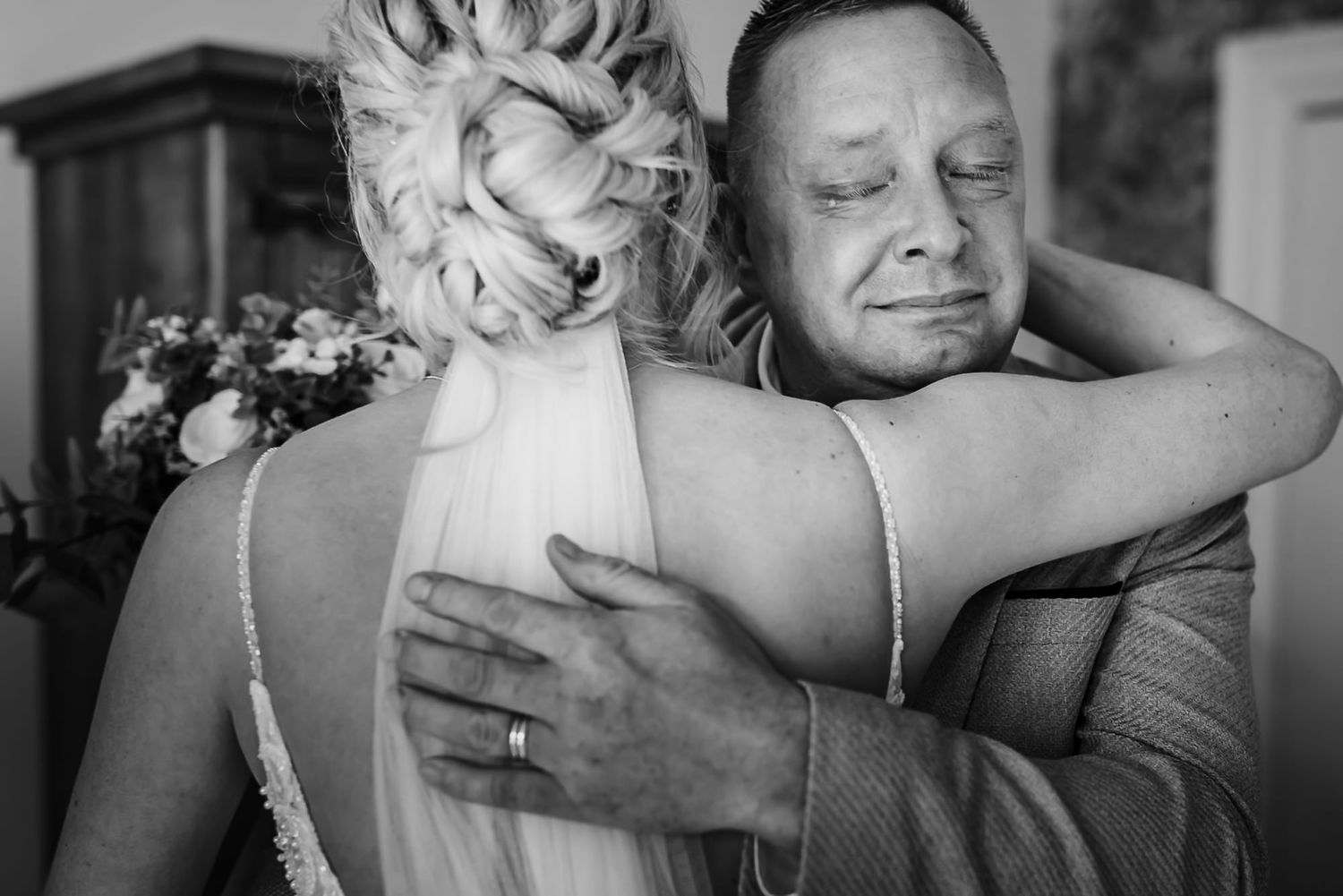 A tender black and white photo captures an intimate embrace between two wedding attendees during an emotional moment.