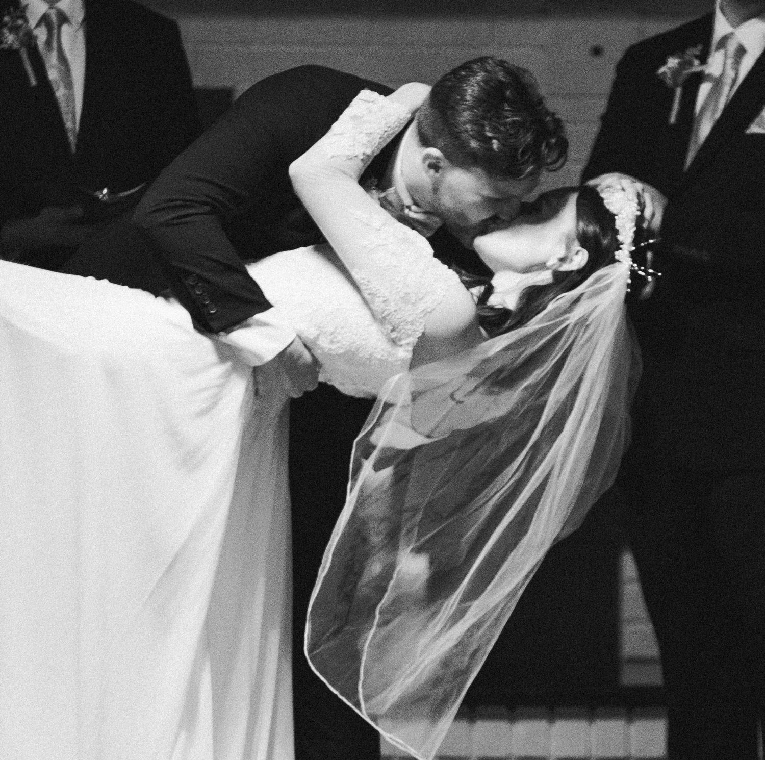 The groom dips and kisses his bride after they exchanged vows and said I do! The photo is in black and white.