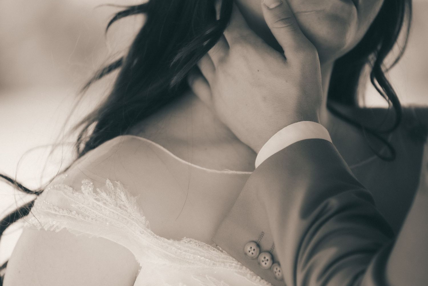 A black and white closeup of the groom gently placing his hand along his bride's jawline.