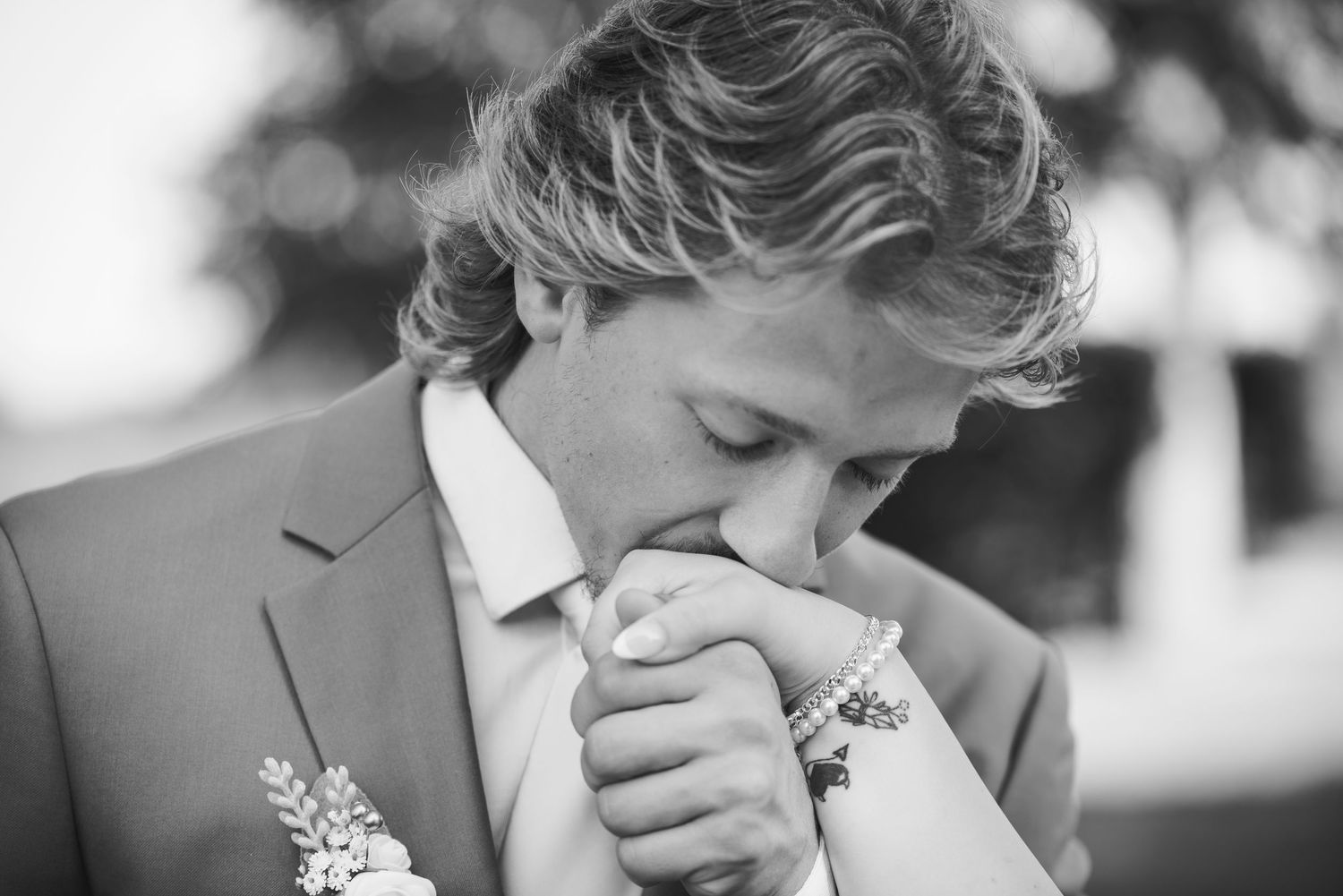 A closeup of the groom holding his bride's hand up to his face and kissing it in black and white.