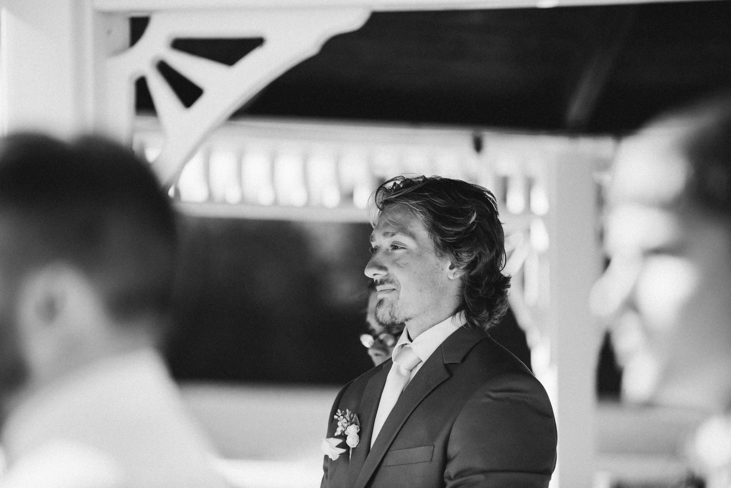 A black and white portrait of the Groom with a light curl to his lips as he anxiously awaits his bride's arrival and descent down the aisle.