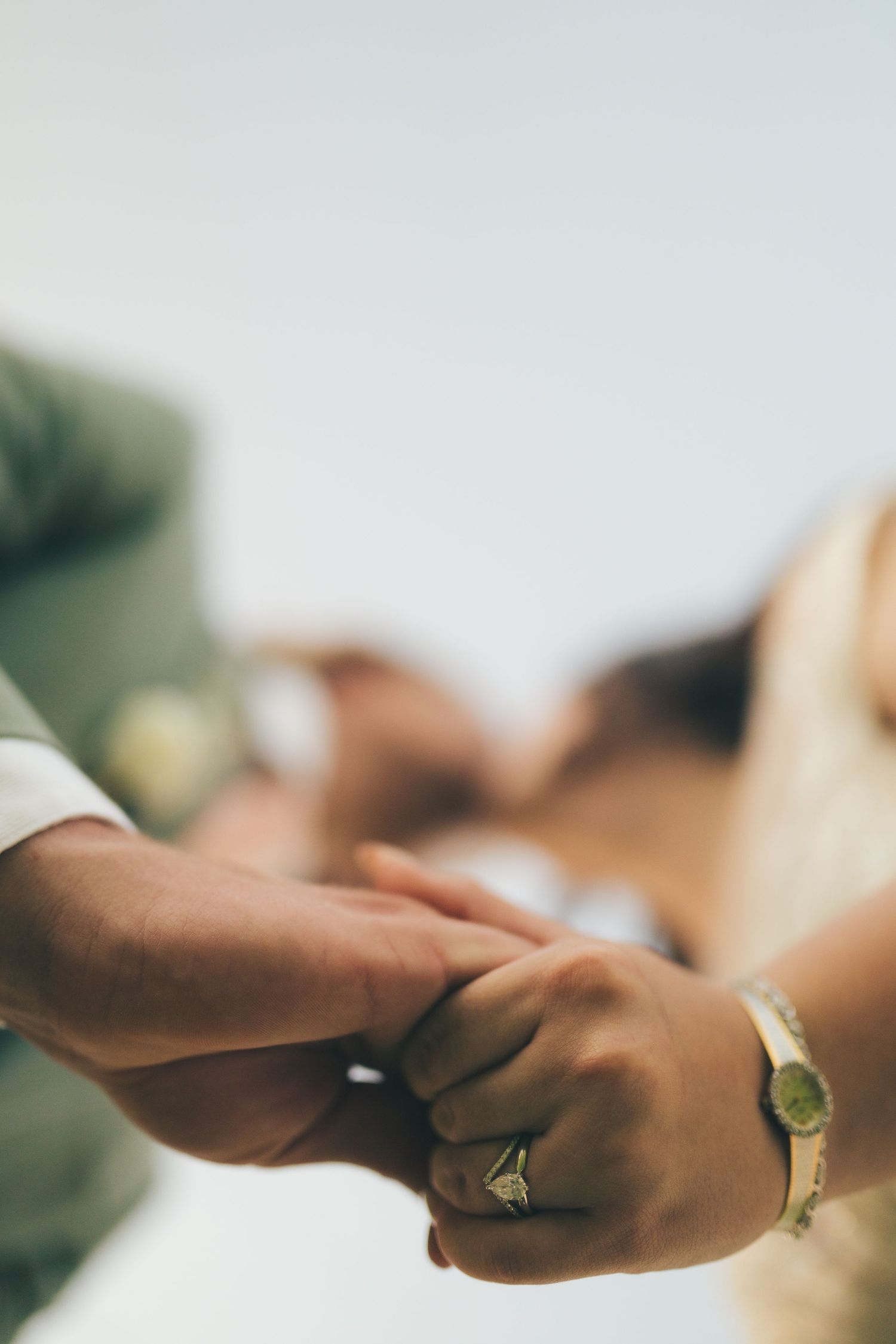 A worms-eye view of the bride and groom holding each other's newly-ringed hands as they kiss above. The kissing is blurred in the background