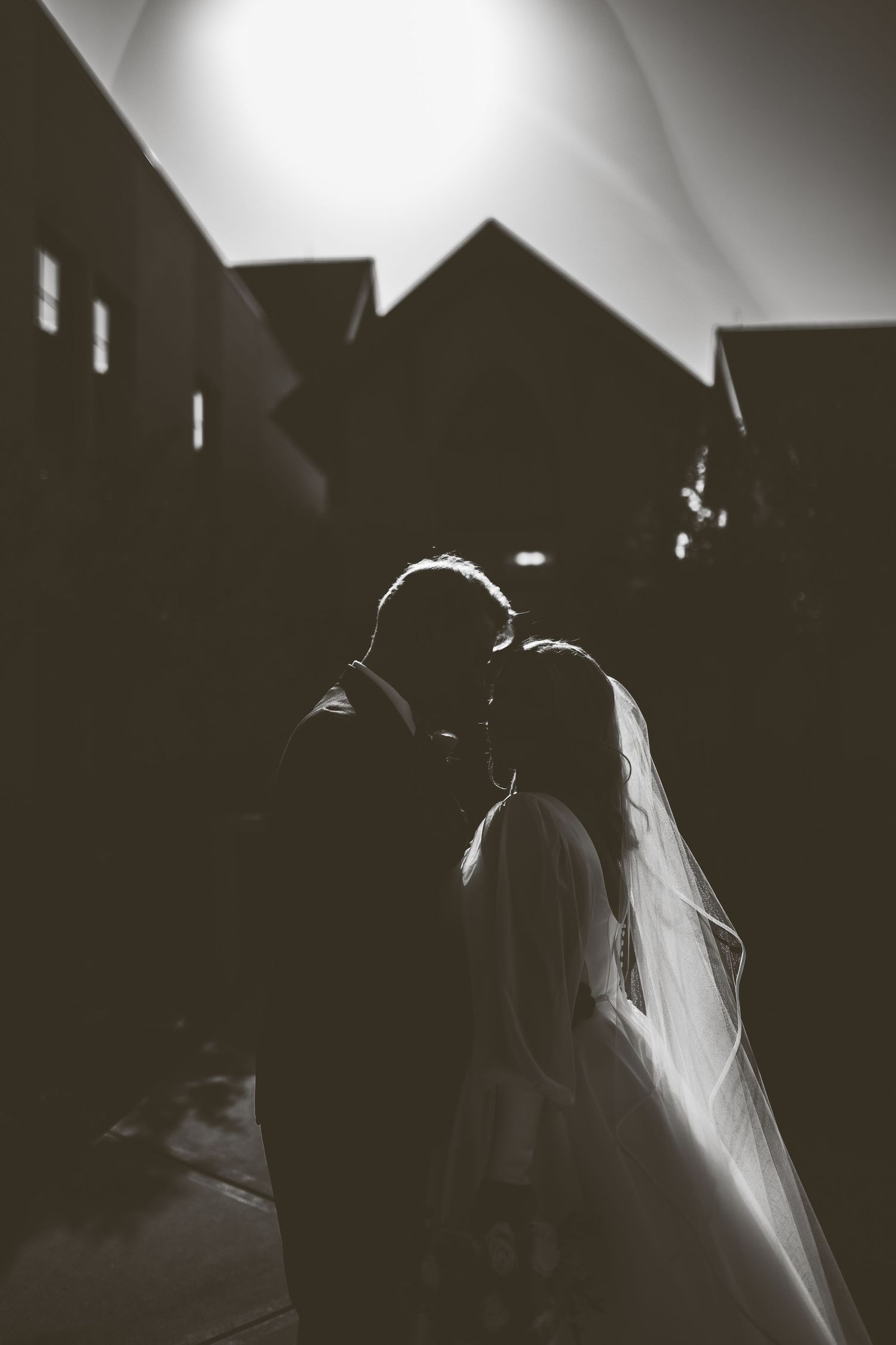 A silhouette and intimate moment of the bride, Sally, and groom, Garrett, before their wedding in the church behind them.