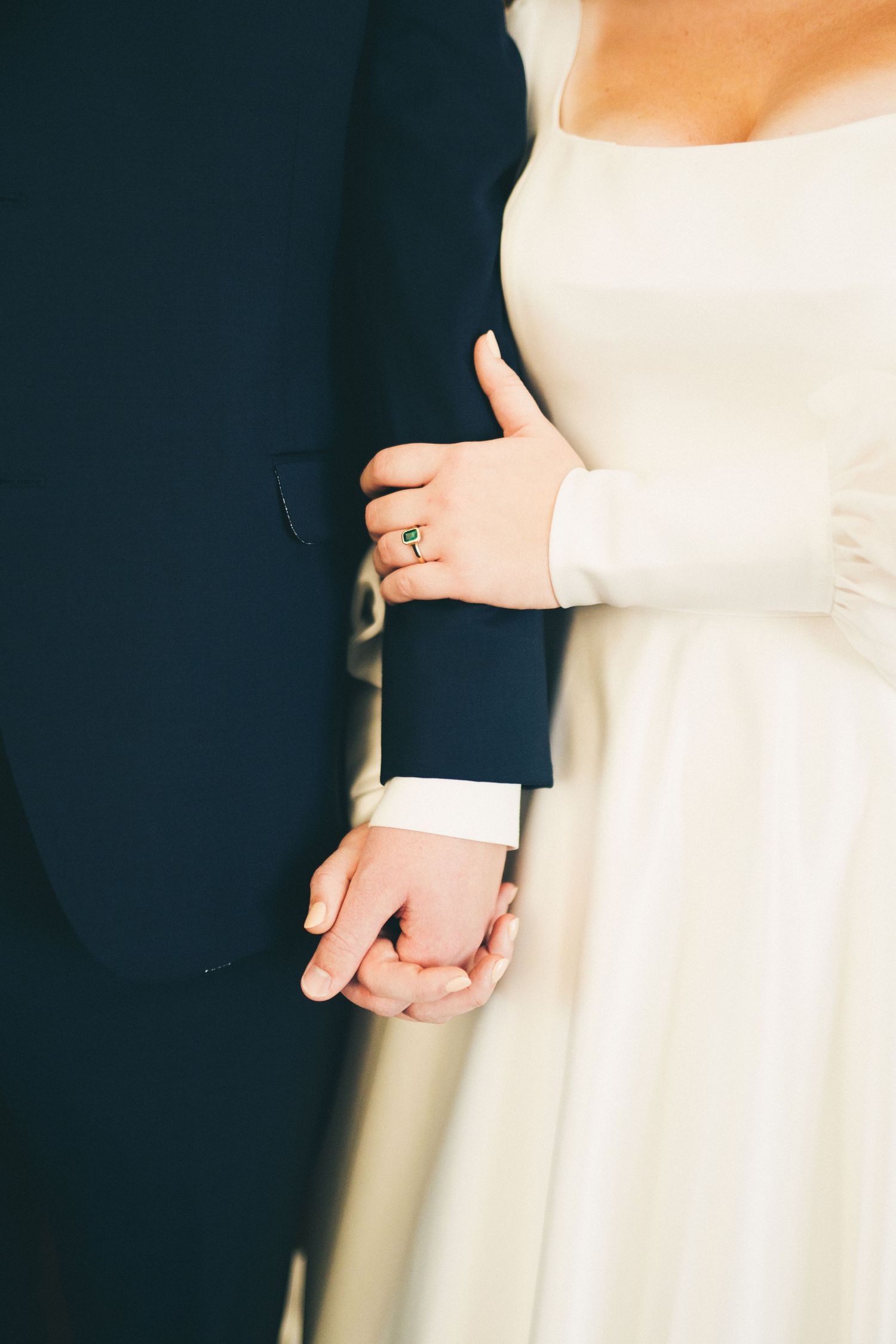 A closeup of the bride and groom, Sally and Garrett, holding hands as Sally holds his arm, showing off her engagement ring and wedding band.