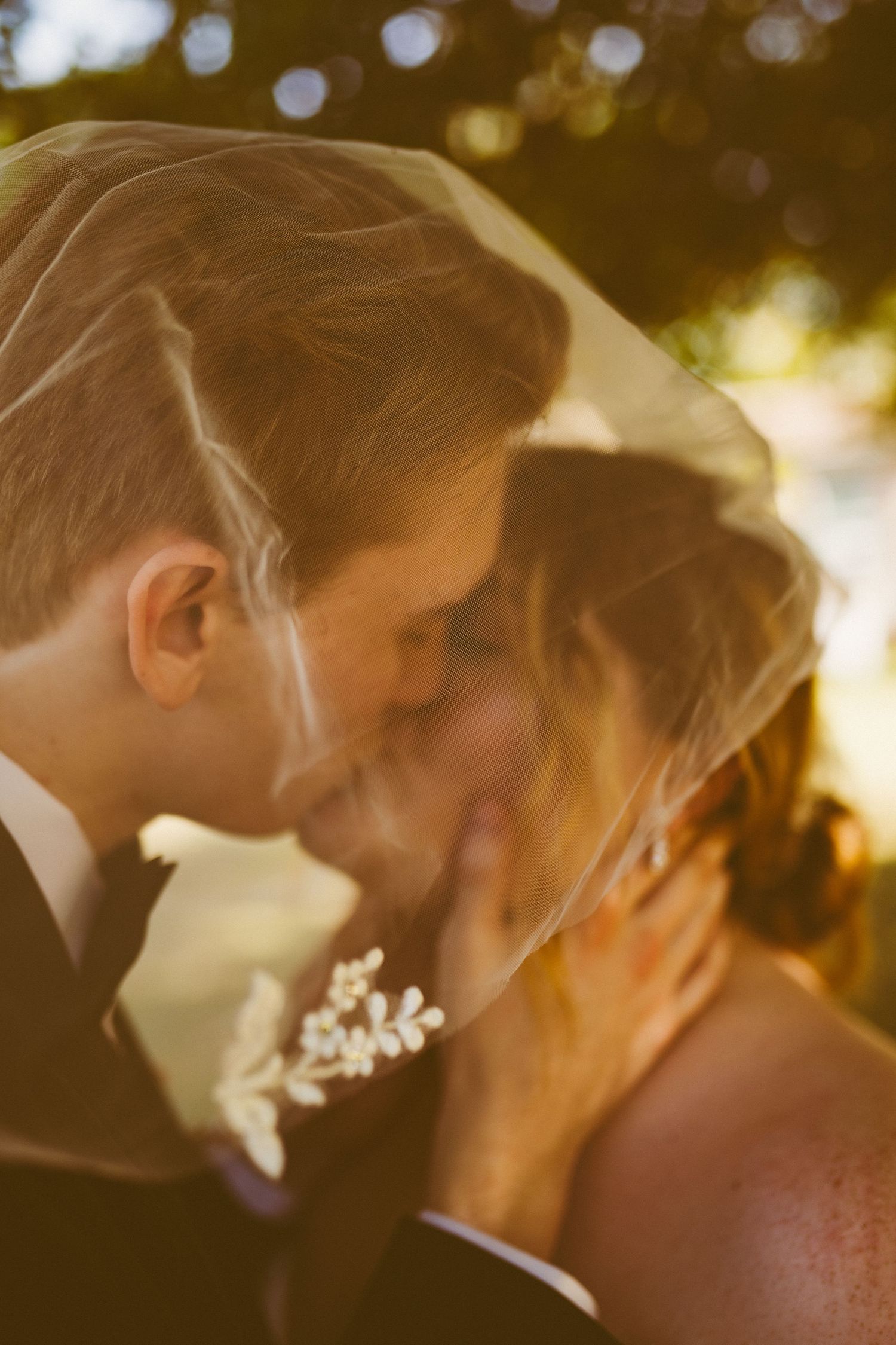 The bride and groom passionately kiss underneath the bride's wedding veil, detailed in floral decals.