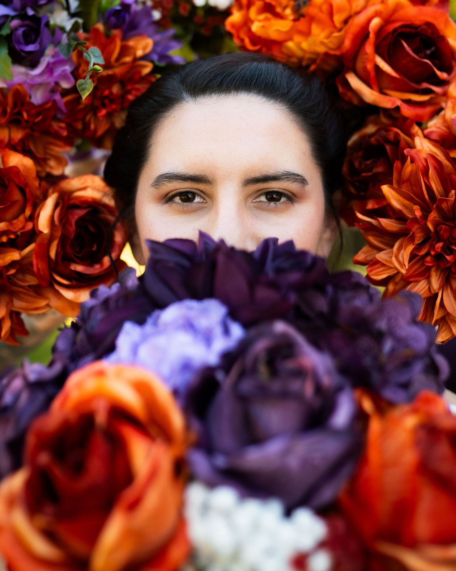 The bride covers her lower face with her bouquet as her bridesmaids surround her face with their bouquets, leaving her in a sea of flowers.