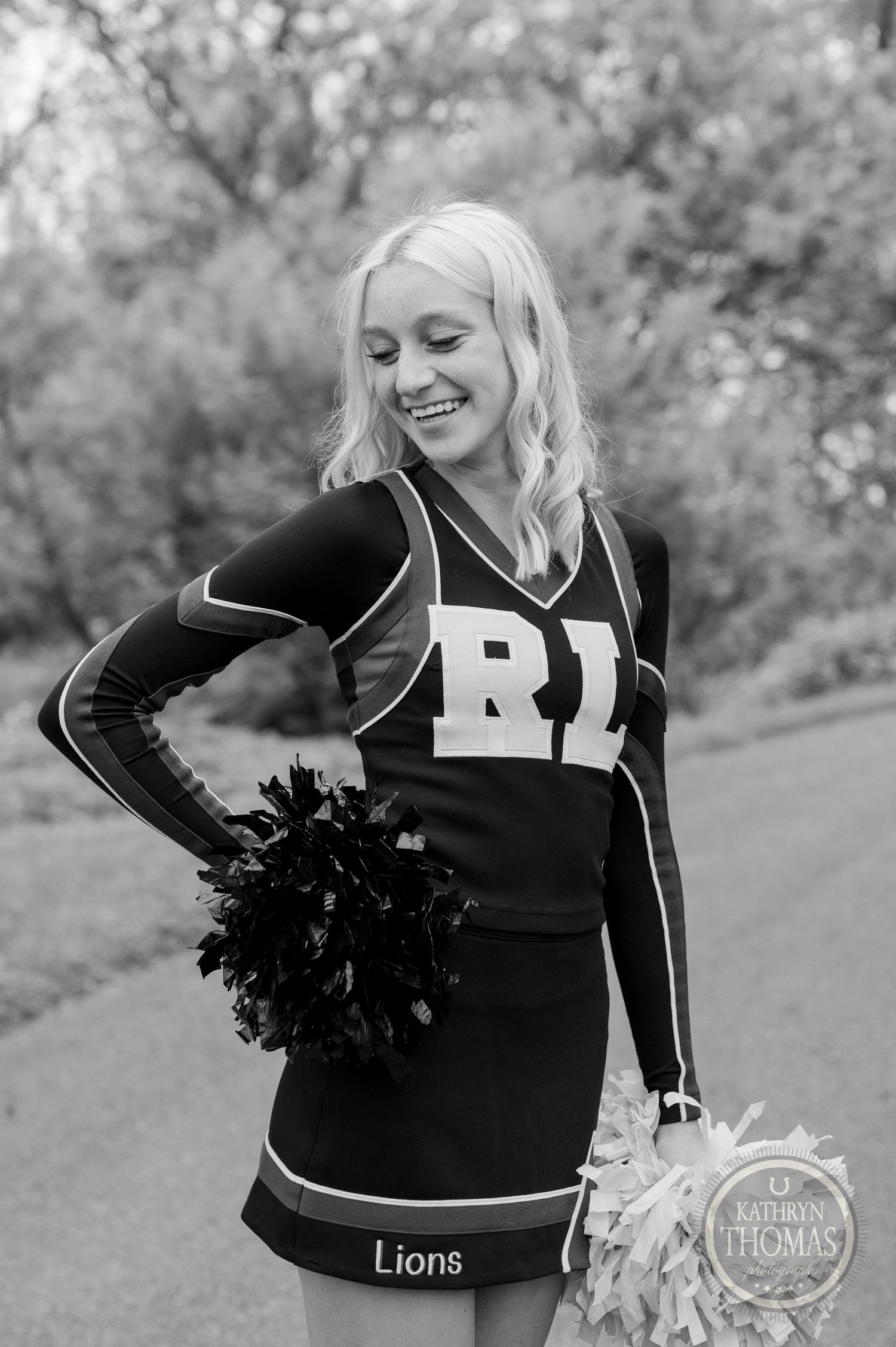 Black and white photo of a cheerleader in a Lions uniform holding pom poms and smiling.