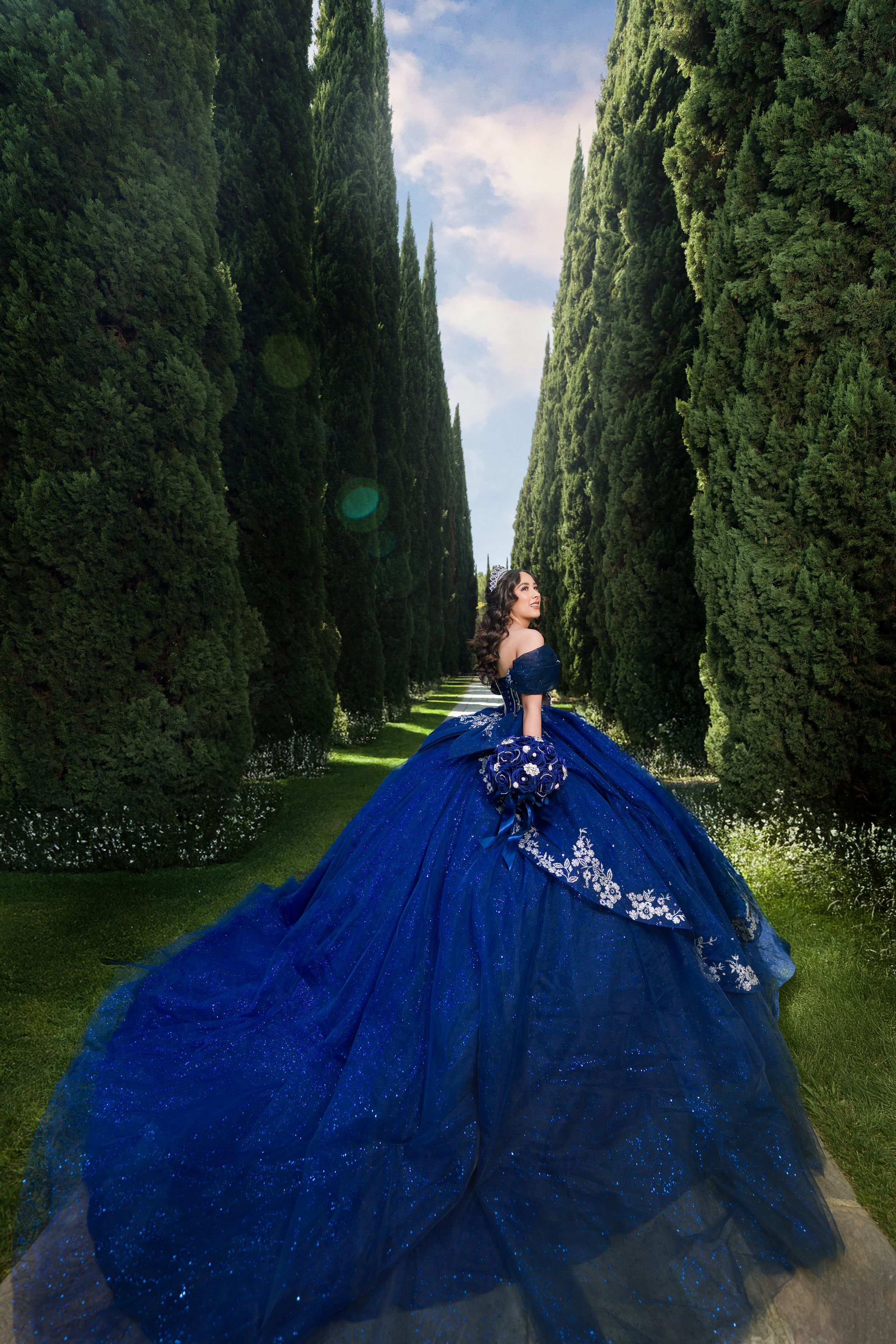 A series of fashion shots showing a stunning royal blue ballgown with silver embellishments in a cypress tree-lined pathway.