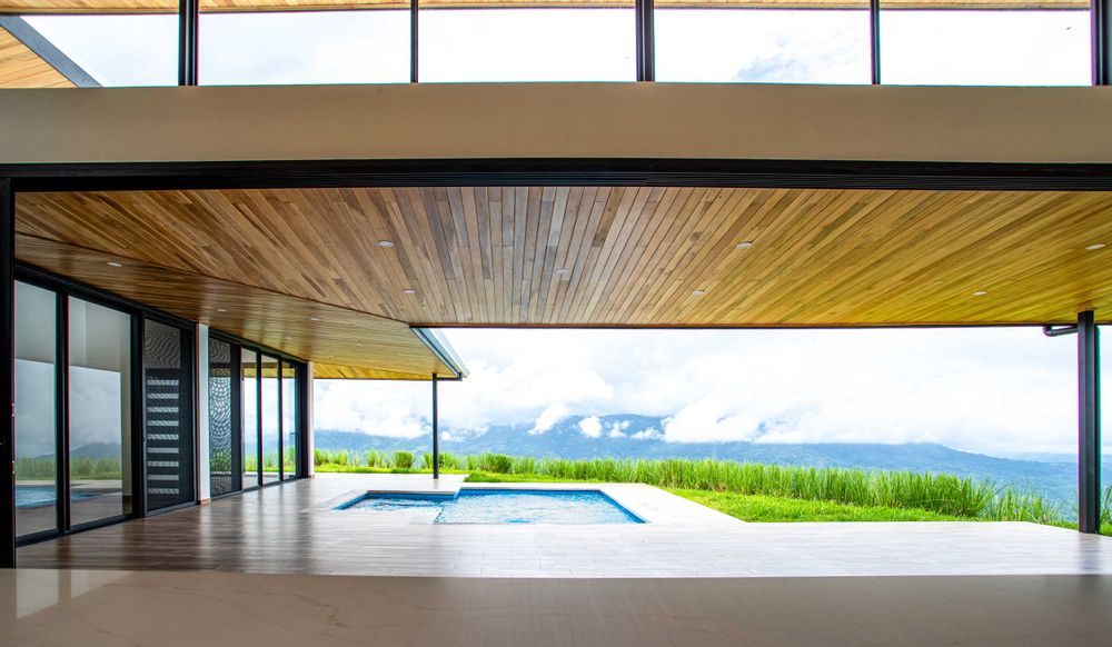 Spacious interior with wooden ceiling and large windows offering panoramic views to the pool property in Atenas, Costa Rica.