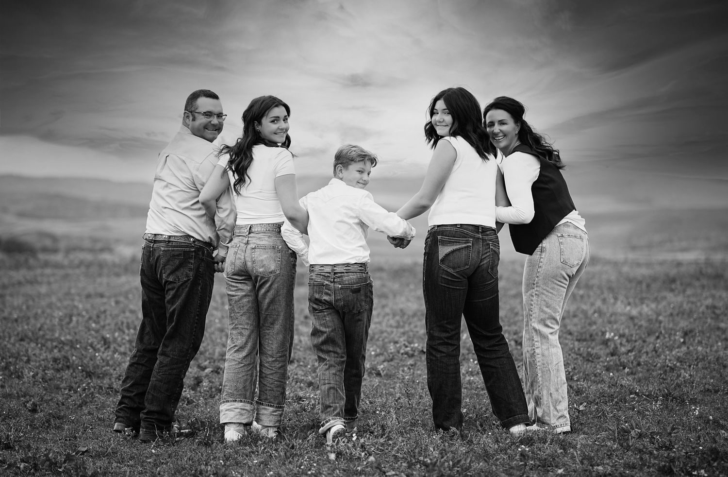 Family holding hands in a circle on grassy hill in black and white photograph.