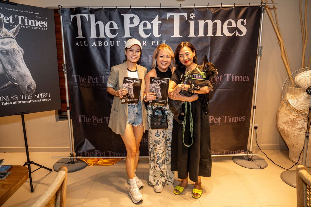 Three people pose together holding beverages in front of a black branded backdrop for The Pet Times.