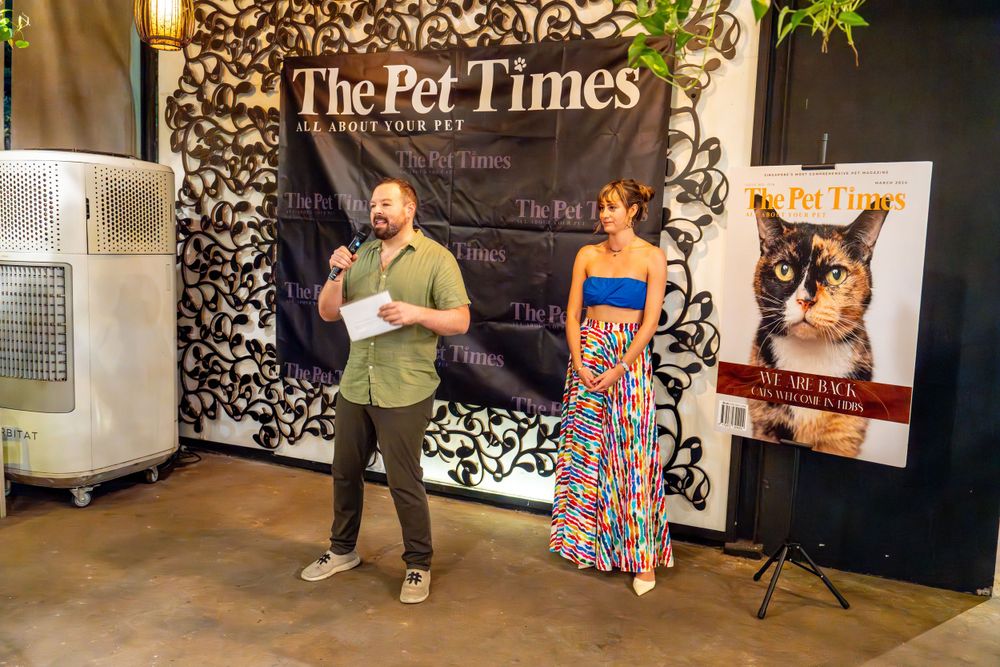 Event setup featuring The Pet Times backdrop display with presenters and a cat portrait banner at a promotional gathering.