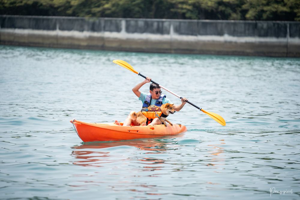 Person kayaking in orange boat on calm water.
