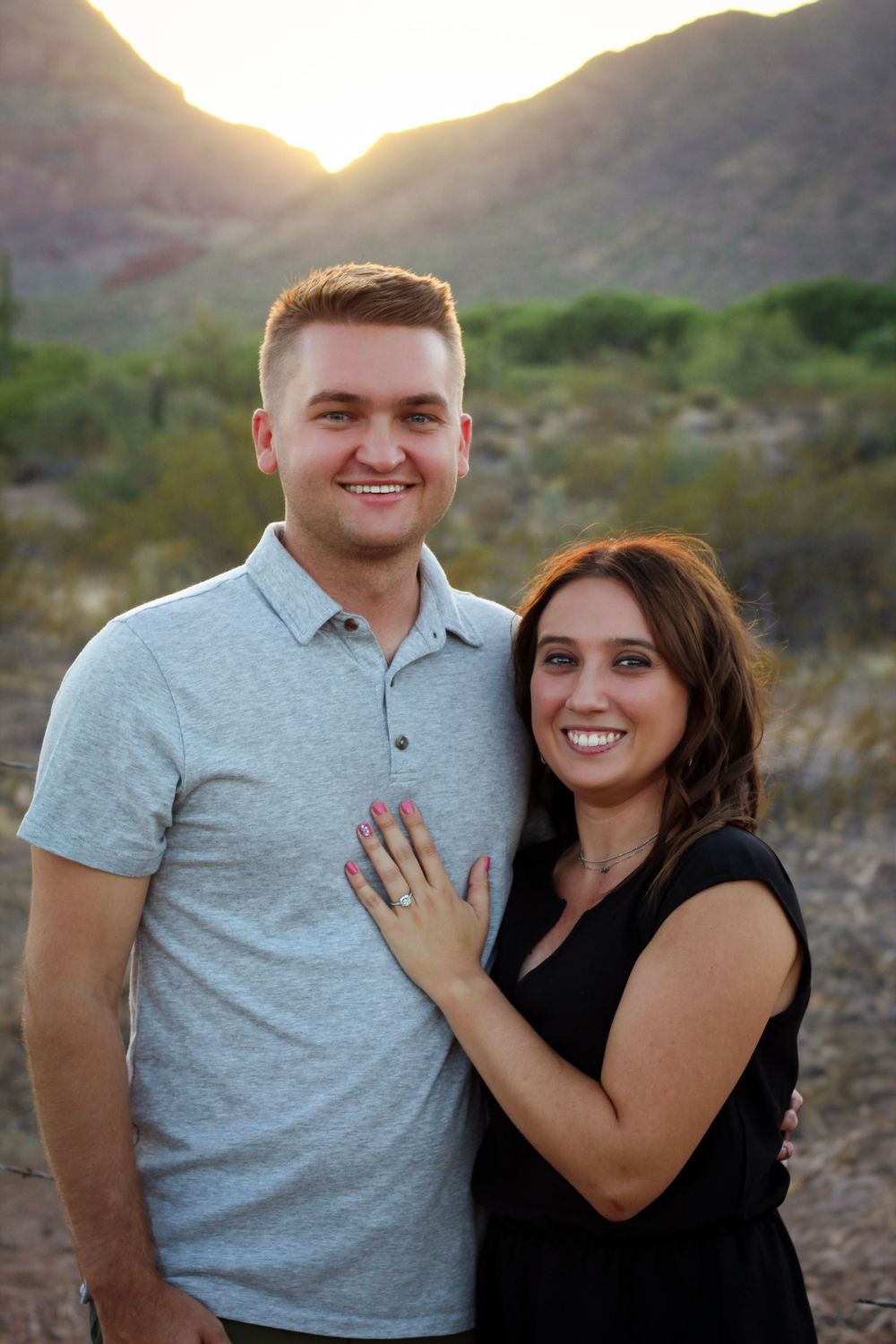 Newly engaged couple smiling at sunset in desert mountain landscape.