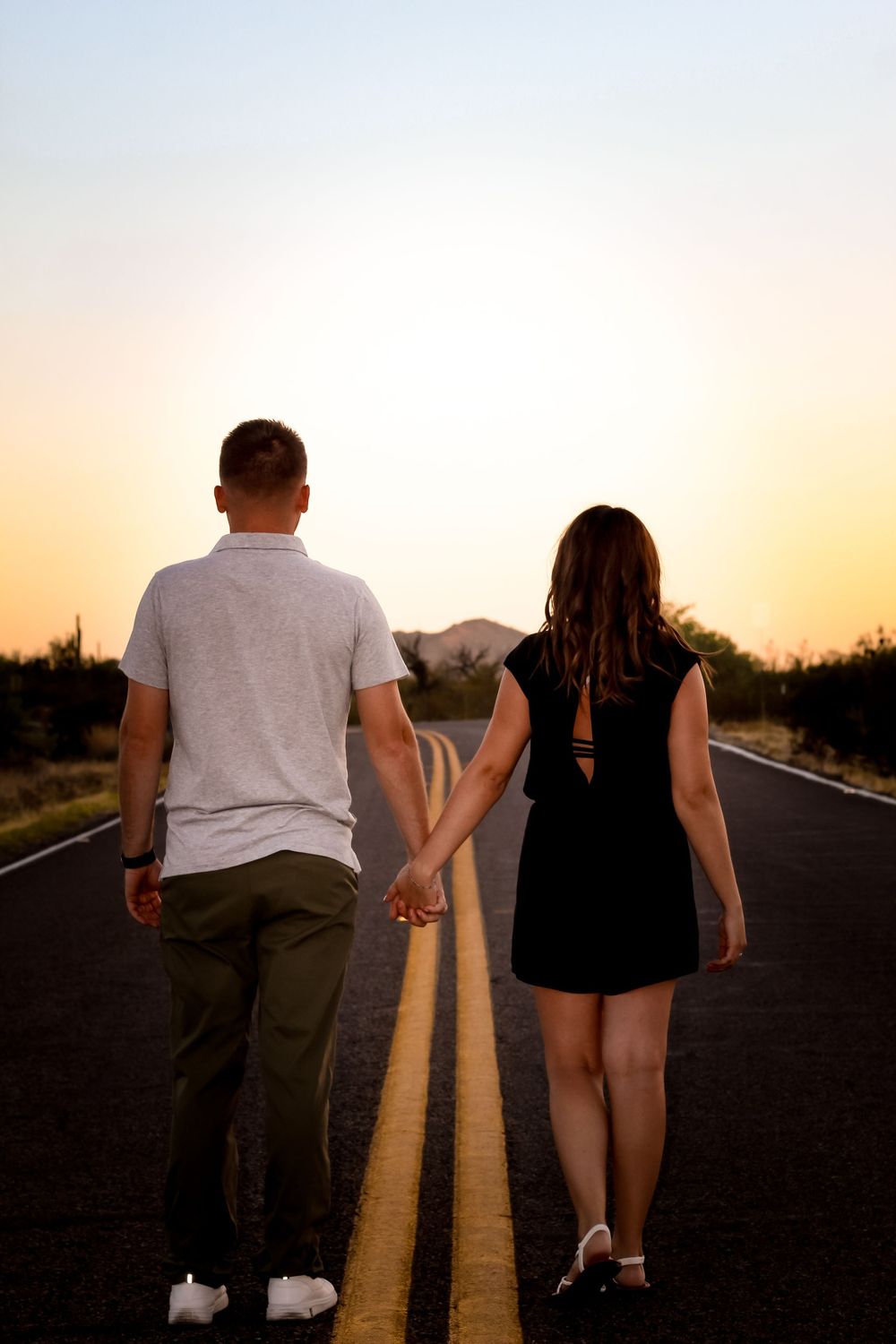 Couple walking hand in hand on empty road during desert sunset.