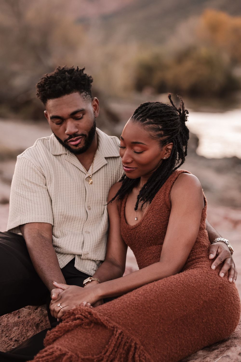 A romantic couple shares an intimate moment while sitting together on rocks during sunset.
