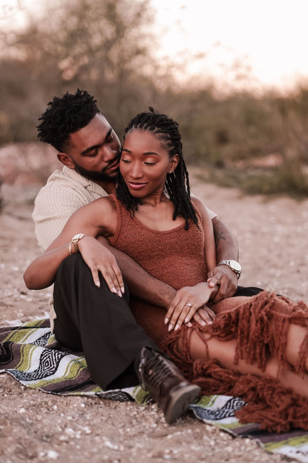 A romantic couple relaxes together on a blanket outdoors during golden hour.