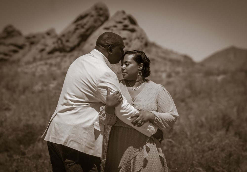 A romantic sepia-toned couple embraces while dancing outdoors with rugged mountains in the background.