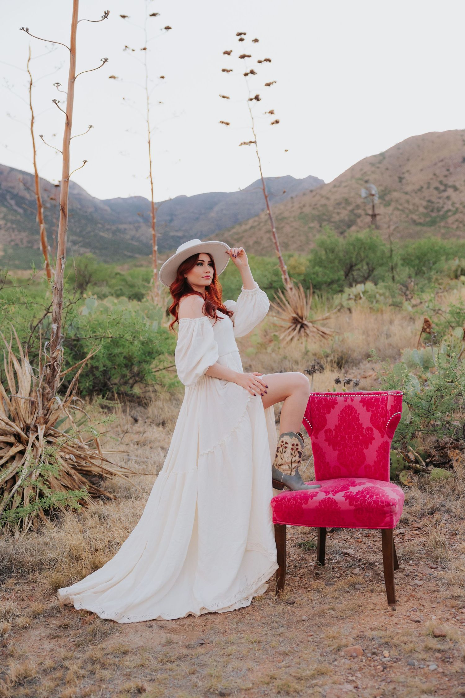 White flowing dress and red vintage chair staged in desert landscape with mountains.