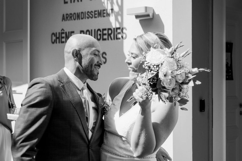 Bride and groom smile at each others in happiness after the wedding. She's holding her bouquet of flowers.