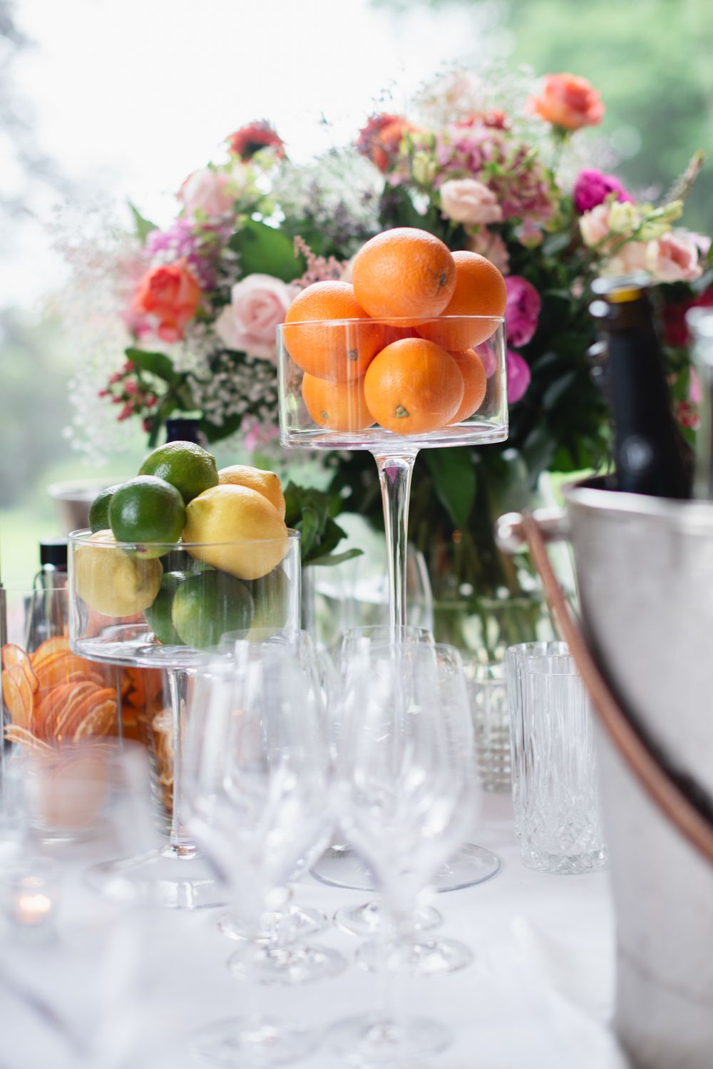 Elegant table setting with citrus fruits in crystal glasses and floral centerpieces.