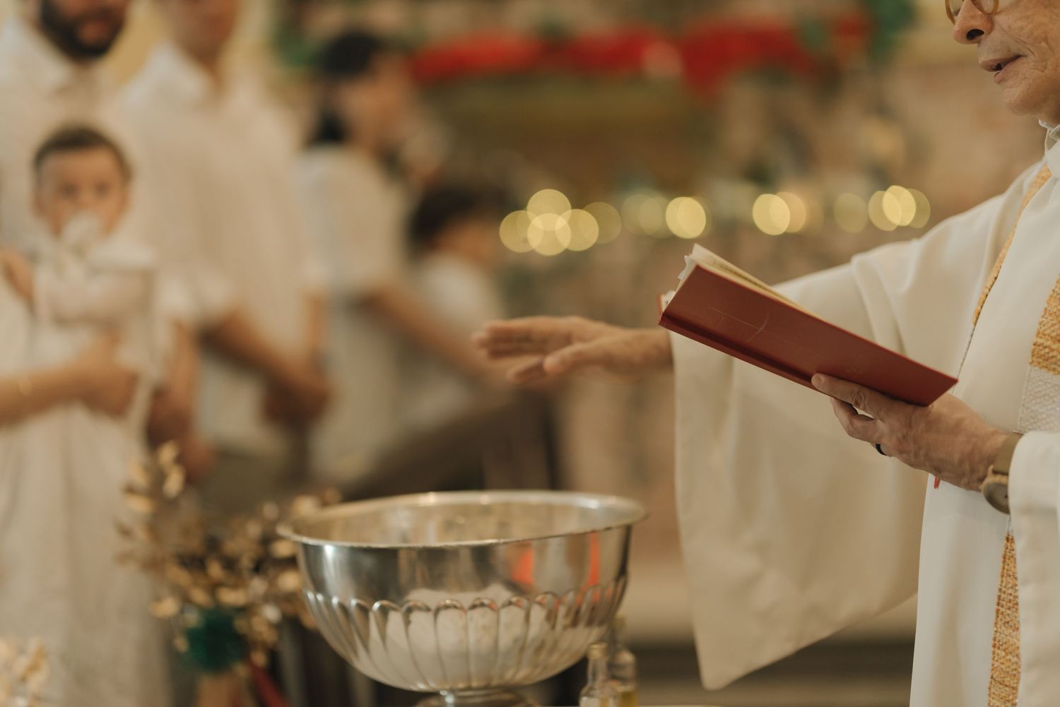 A priest performs a religious ceremony with a silver baptismal font.
