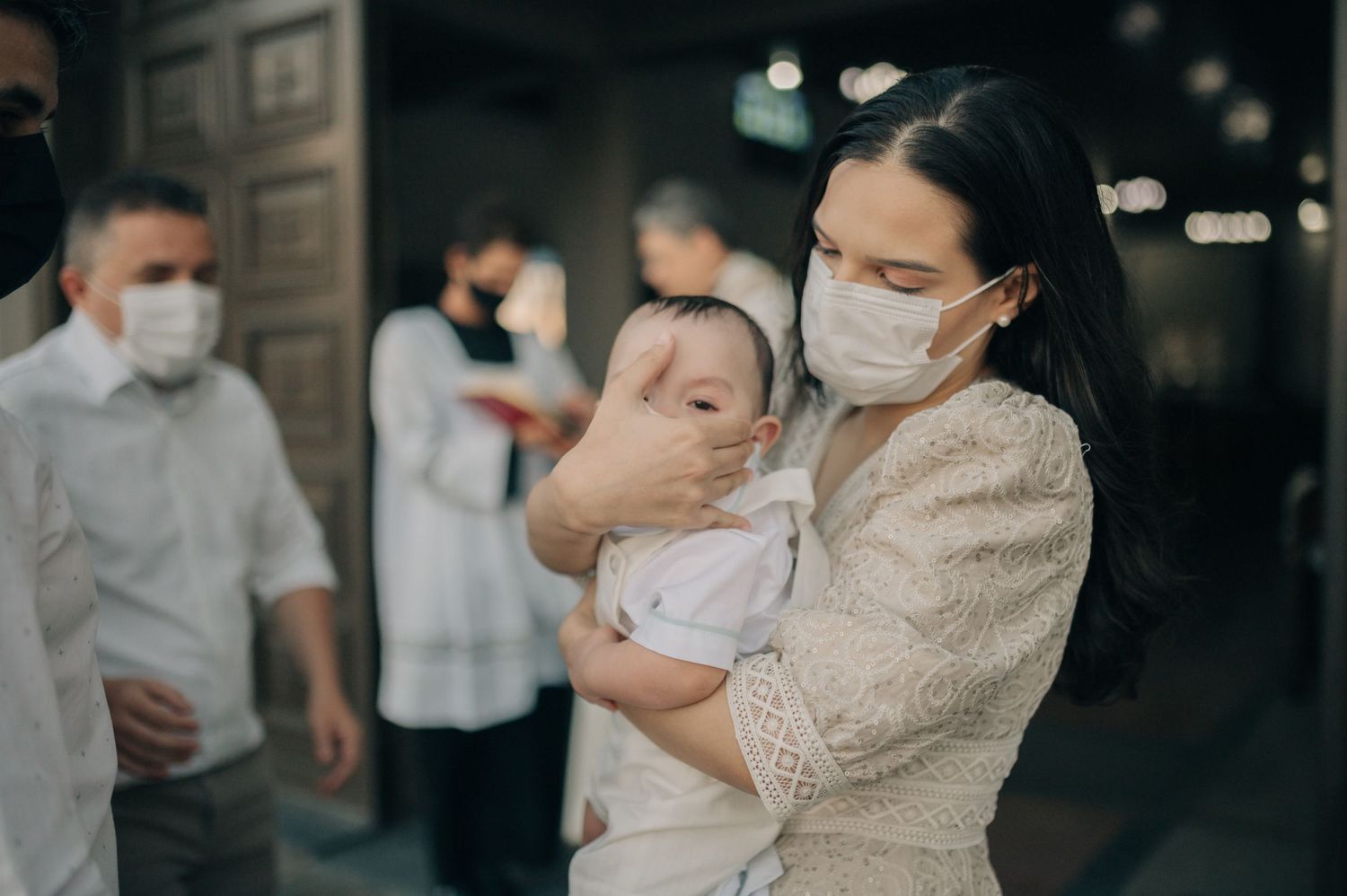 People wearing protective masks gather inside a dimly lit building during what appears to be a ceremony.