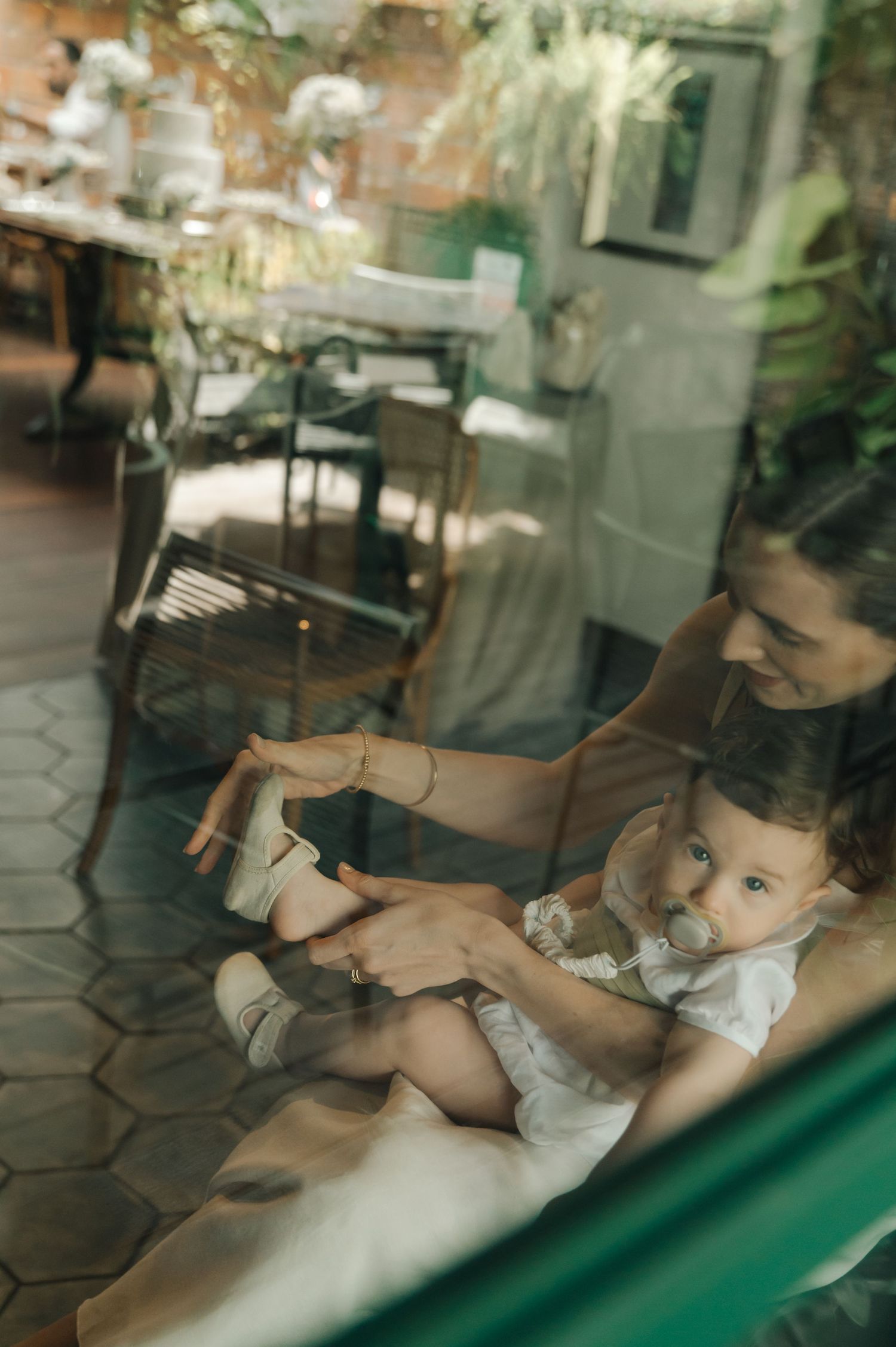 Reflection through glass shows a tender moment during a baptism ceremony.