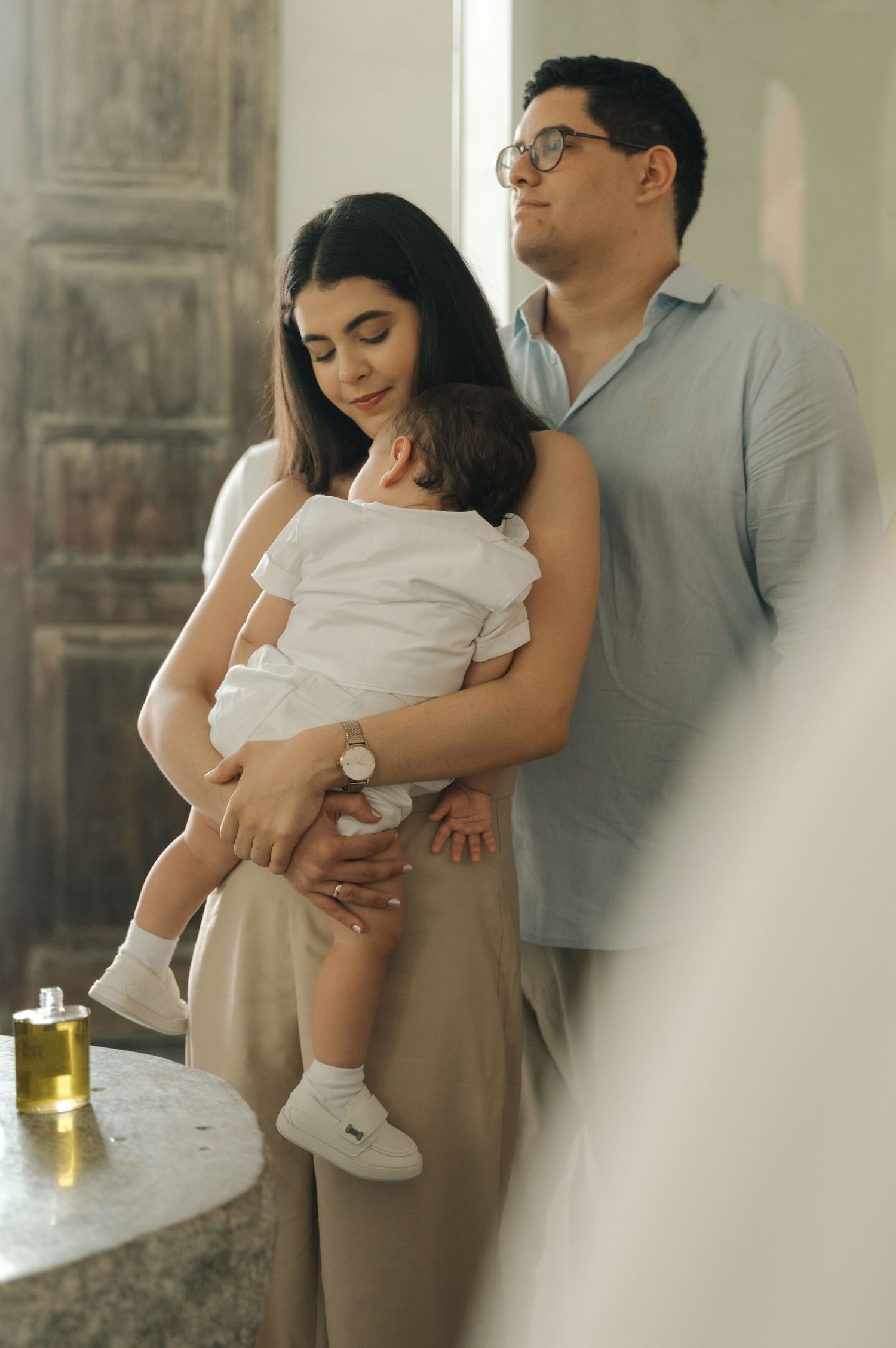 Couple in casual attire embracing with their baby in white clothing.