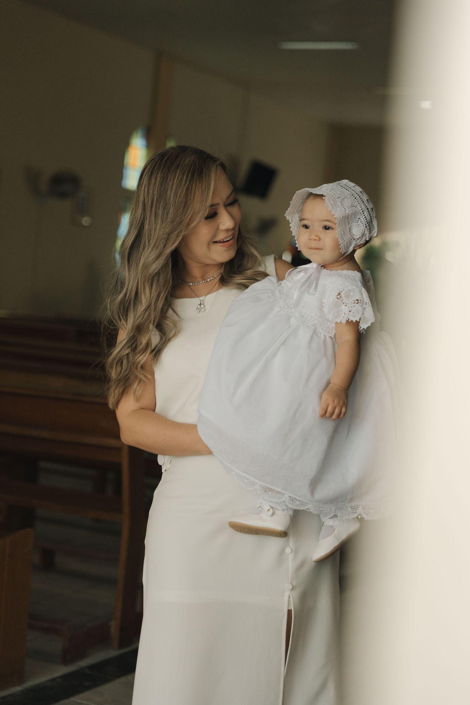 A small child wearing traditional white baptismal gown is held in a church setting.