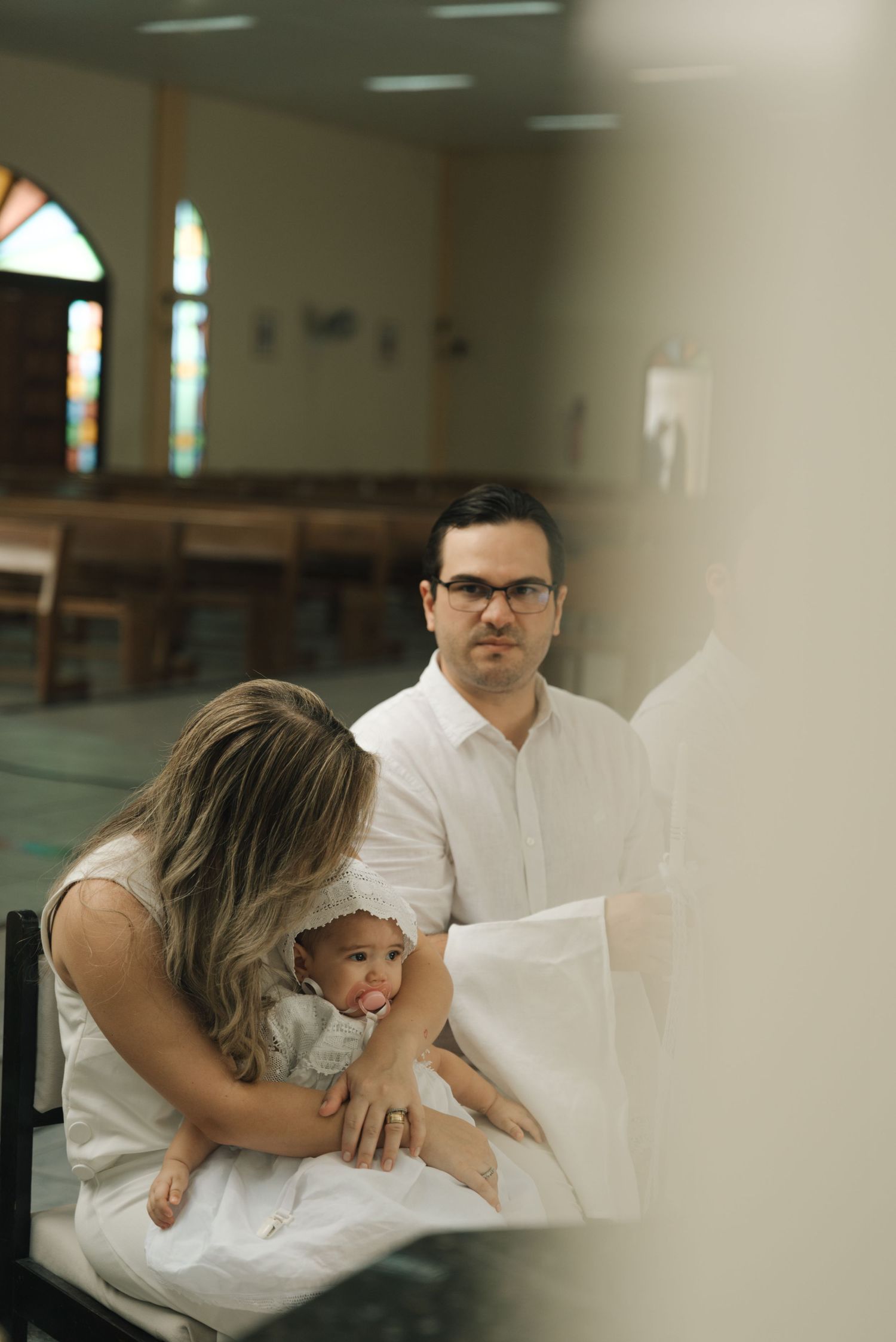 Family dressed in white sharing an intimate moment on church bench.