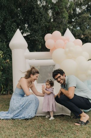 Family sharing playful interaction outdoors on grass with white and peach colored balloons in garden setting.