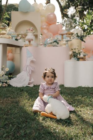 Party scene with delicate pink and white decorations, balloon arches, cutout swans, and pastel displays in an outdoor garden setting.