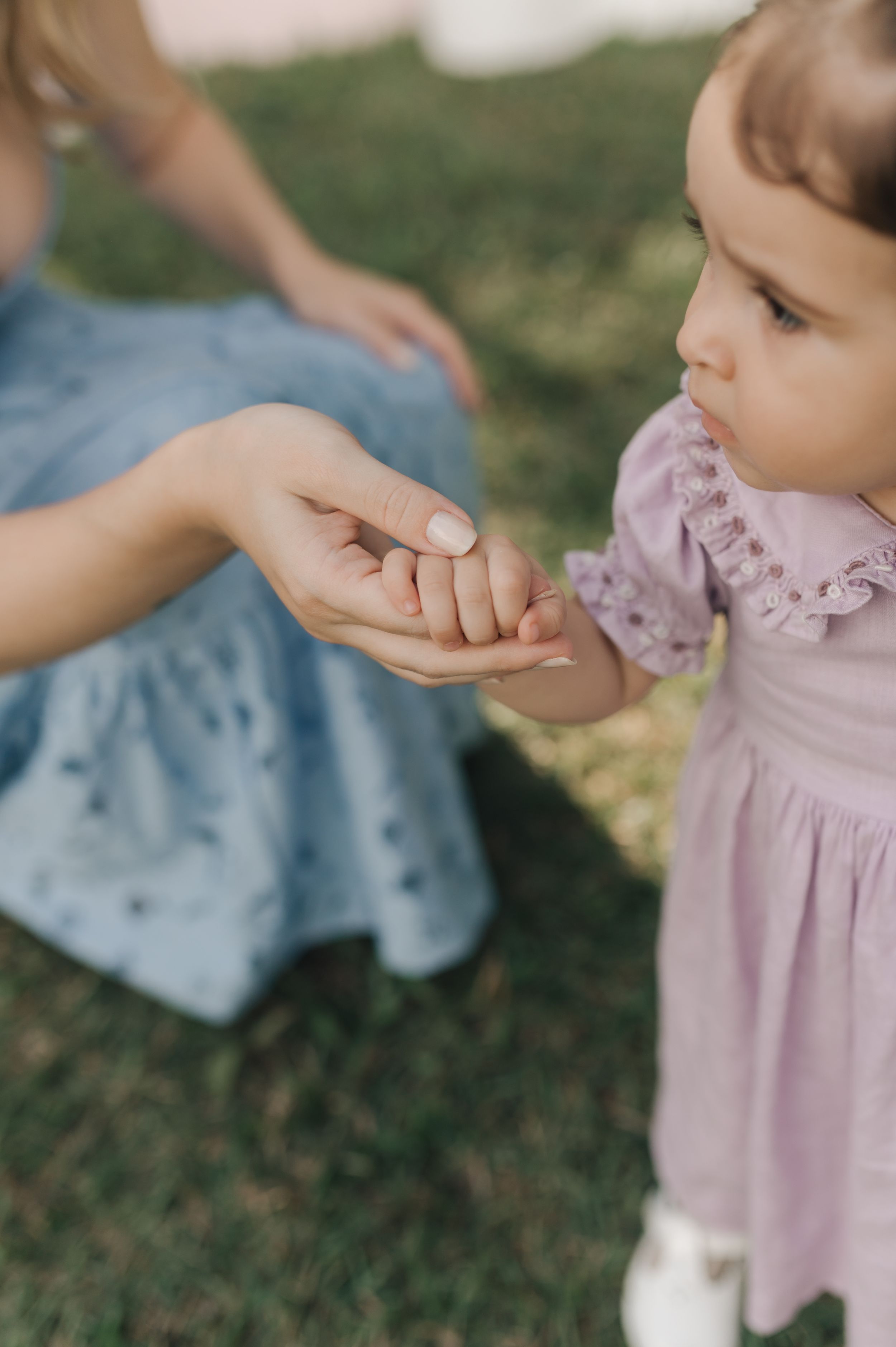 Small child in pink dress holding hands with someone in blue clothing while standing on grass.